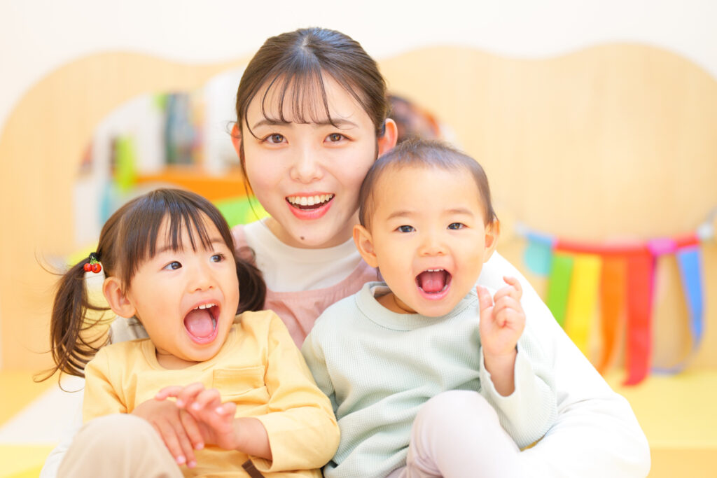 保育室で女性保育士と笑顔の二人の子ども