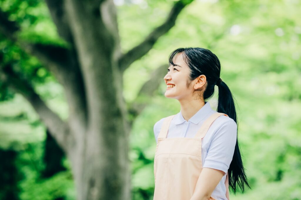 エプロンをつけた女性が木のある屋外で微笑む
