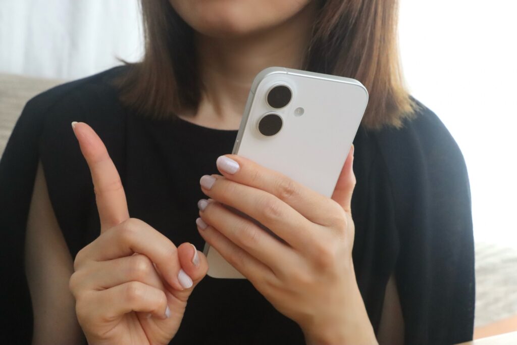スマホを持って人差し指を立てる女性