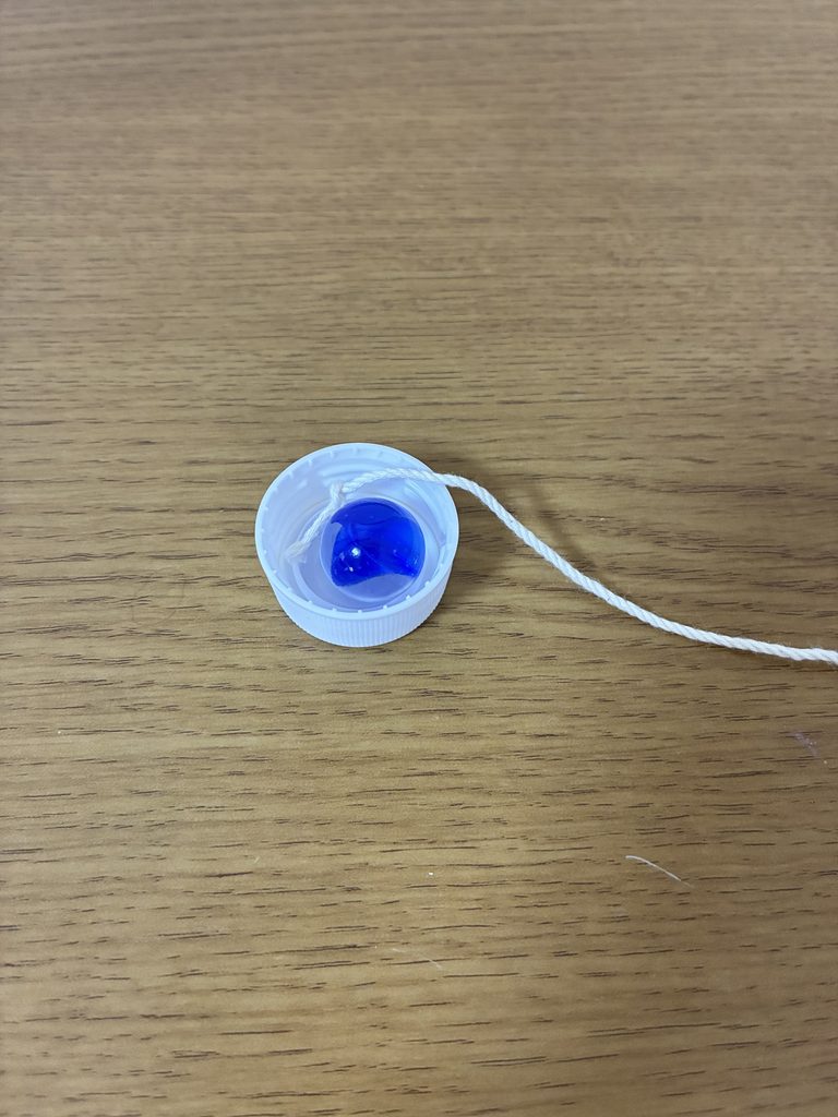 ペットボトルキャップにビー玉とタコ糸の結び目を入れているところ