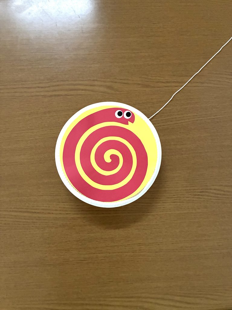 紙皿の両面に黄色の丸と赤いヘビを貼ったところ